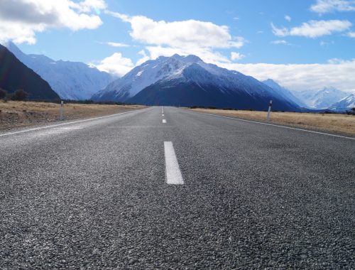 gray asphalt road near mountain range under blue sky during daytime